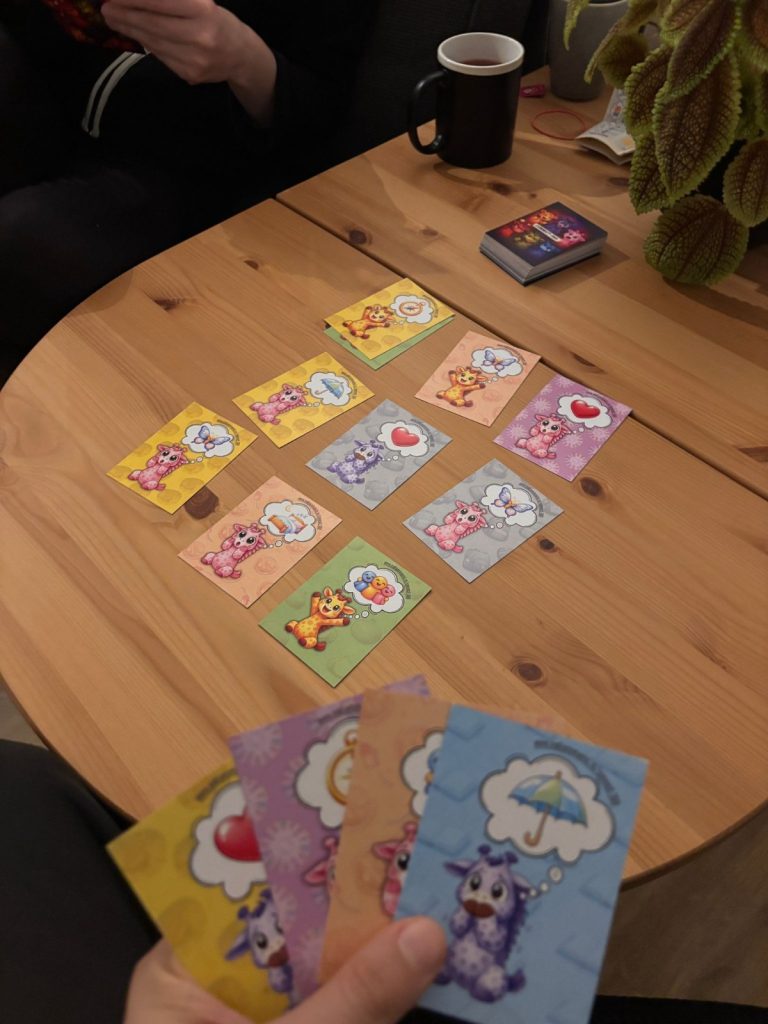 Carduri ilustrate cu girafe reprezentând emoții și nevoi, din jocul Connect-360, așezate pe masă și ținute în mână